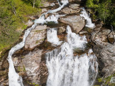 Norveç 'in dağlarındaki yemyeşil yemyeşil dağların ortasındaki kayalık çıkıntılardan süzülen güçlü çağlayan şelalenin nefes kesen hava manzarası..