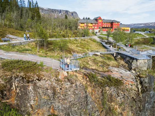 EIDFJORD, NORWay - 19 Mayıs 2025: Voringsfossen şelalesindeki tarihi Fossli Oteli 'nin arka planındaki izleme platformunda turistlerin insansız hava aracı görüntüsü.