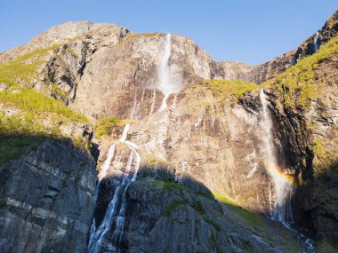 Norveç dağlarındaki kayalık uçurumlardan akan şelalelerin sersemletici hava aracı görüntüsü. Su püskürtüsünde gökkuşağı var..