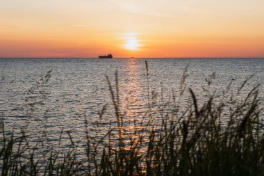 Baltık Denizi 'nin sakin suları üzerinde altın bir günbatımı, bir petrol tankerinin karanlık siluetleri ve bir kargo gemisinin ufukta göründüğü yerde, Estonya kıyılarından bakıldığında,.