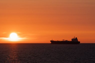 Günbatımında Baltık Denizi 'nin büyüleyici deniz manzarası. Ufuktaki bir geminin silueti parlak turuncu bir gökyüzüne ve batan güneşe karşı.