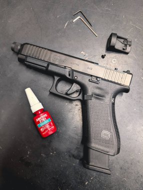 TALLINN, ESTONIA 19 HAZİRAN 2025 Bir Glock 47 9x19 kalibre tabanca kırmızı nokta görüşü kurma sürecinde. Bağlama araçları ve Loctite iplik dolabı masanın üzerinde..
