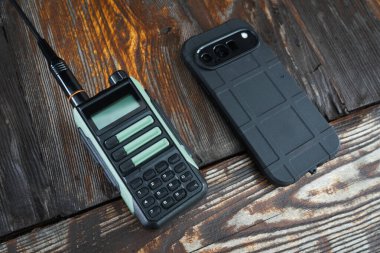 İki farklı iletişim türü: portatif çift yönlü bir radyo ve ahşap bir masada modern dayanıklı bir akıllı telefon. Radyo ve hücresel iletişim arasında seçim yapma kavramı..