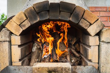Fire burns brightly in a traditional wood-fired brick oven. An outdoor oven for cooking pizza and bread.