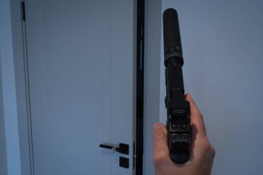 Birinci şahıs bakış açısı: elinde susturucu tabanca olan bir adam odaya girmeye hazırlanıyor. Gerilim ya da casusluk konsepti.