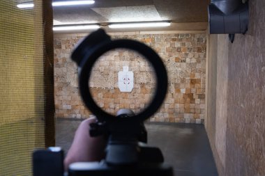 Birinci şahıs bakış açısıyla modern bir tüfeği, kapalı bir atış poligonunda kağıttan bir hedefe nişan almak..