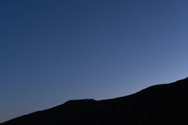 Açık yıldızlı gökyüzüne karşı karanlık bir dağ silueti olan minimalist bir gece manzarası. Sakinlik ve sükunet kavramı için atmosfer arkaplanı.