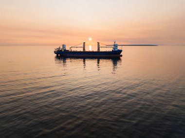 Açık denizde destansı turuncu bir gün batımına karşı bir kargo gemisinin siluetinin nefes kesici görüntüsü..