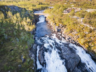 Norveç yaz ormanlarındaki eski bir taş köprünün altındaki kayalık bir kanyonda güçlü bir şelale ve nehrin resimli hava görüntüsü..