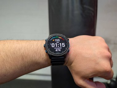 TALLINN, ESTONIA - 27 Haziran 2025: Antrenman sırasında bir adamın bileğindeki bir Garmin akıllı seğirmesinin yakın çekimi. Saat ekranında kalp hızı, zamanlayıcı ve kalori yanığı gibi sağlık verileri gösterilir.