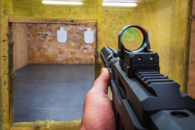 Yakın plan: Bir nişancının eli, atış poligonunda aktif kırmızı nokta görüşlü bir taktik karabina tutar..