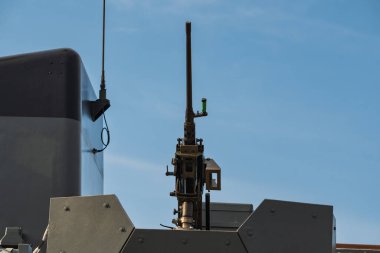 Geniş kalibreli bir savaş makineli tüfeği zırhlı bir kulede, açık mavi gökyüzüne karşı modern askeri teçhizata monte edilmiş..