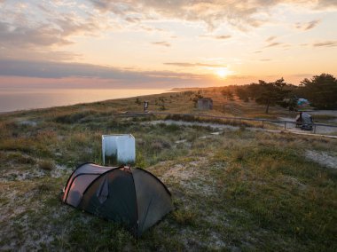Deniz kıyısındaki kum tepeciğindeki bir kamp çadırının hava aracı görüntüsü güzel bir günbatımı sırasında.