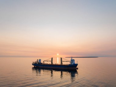 Güneş doğarken Baltık Denizi 'nin sakin sularına demir atmış büyük bir kargo gemisinin insansız hava aracı görüntüsü..