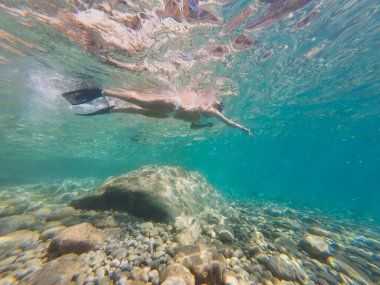 Bir kadın Saint-Jean-Cap-Ferrat, Fransa 'da bir çakıl taşının üzerindeki turkuaz denizde şnorkelle yüzüyor..