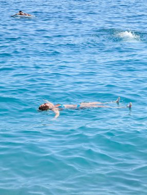 Genç bir kadın bir yaz günü açık mavi denizde sırtüstü uzanıyor ve dinleniyor..