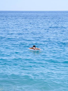 Yalnız bir insan, güneşli bir günde sakin, engin mavi denizde huzur içinde yüzen şişme bir yüzüğün üzerinde rahatlar..