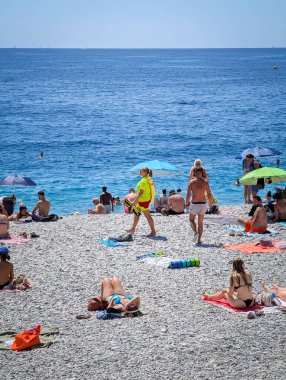 Güzel, FRANCE - 7 Ağustos 2025: Sarı üniformalı bir kadın cankurtaran turistler güneşlenirken ve Fransız Rivierası 'nın yaz gününün tadını çıkarırken kalabalık çakıl taşı plajlarında devriye geziyor..