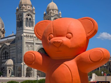 Marsilya, FRANCE - 31 Temmuz 2025: Güneşli bir yaz gününde ünlü Marsilya Katedrali önünde dev bir turuncu oyuncak ayı heykeli.