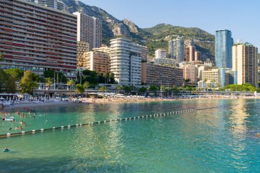 MONTE CARLO, MONACO - 7 AĞUSTOS 2025: Yüzücüler Larvotto Sahili 'nde Akdeniz' in keyfini çıkarırken, Monte Carlo 'nun ünlü modern silueti geride yükseliyor..
