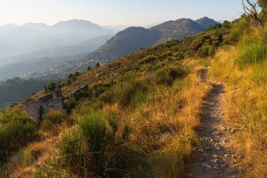 Altın saat güneş ışığı, Fransa 'ya tepeden bakan Fransız Rivierası' nın güzel dağlarında kırsal bir yürüyüş yolunu aydınlatıyor..