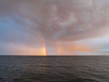 Baltık Denizi 'nin dingin ve engin sularının üzerindeki dramatik günbatımı bulutlarından muhteşem bir çift gökkuşağı doğar..