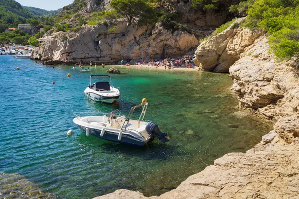 Marsilya, FRANCE - 29 Temmuz 2025: İnsanlar açık turkuaz Akdeniz sularına demirlemiş motorlu teknelerle Calanques Ulusal Parkı 'ndaki tenha bir plajda sıcak bir yaz gününün tadını çıkarıyor.