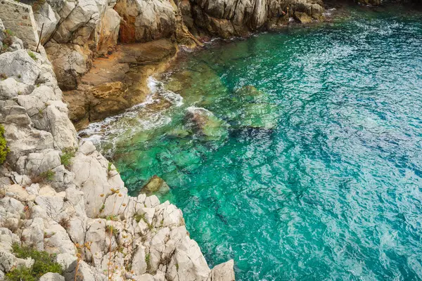 Engebeli kayalıklar, Saint-Jean-Cap-Ferrat, Cote d 'Azur, Fransa' daki manzaralı bir koyda kristal berraklığında turkuaz Akdeniz ile buluşuyor..