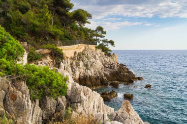 Saint-Jean-Cap-Ferrat yarımadasının kayalık uçurumlarındaki güzel Akdeniz, Fransız Rivierası manzaralı sahil yolu..