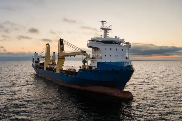 Gün batımında sakin Baltık Denizi 'nde uçan vinçleri olan genel bir kargo gemisinin insansız hava aracı görüntüsü..