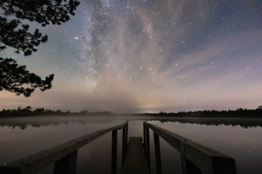 Estonya 'daki ahşap bir iskeleden sakin ve sisli bir bataklık gölü üzerinde yükselen Samanyolu' nun çarpıcı görüntüsü..