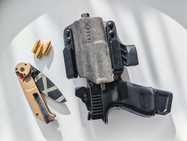 BALTICS - OCTOBER 2, 2025: IWB kılıfında bir Glock tabanca ve katlanan bir Extrema Oranı bıçak odaklı bir günlük taşınma düz yatıyordu.