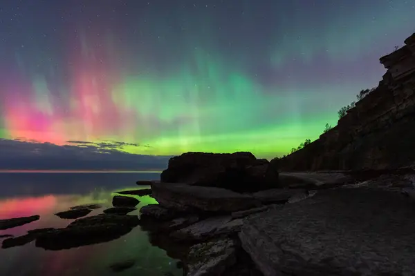 Estonya 'daki kayalık Baltık Denizi kıyısında dans eden göz kamaştırıcı pembe ve yeşil Aurora Borealis (Kuzey Işıkları) gösterisi.