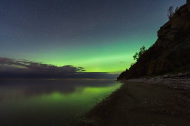 Yeşil aurora borealis, sakin Baltık Denizi ve Estonya 'daki Paldiski uçurumunun üzerinde yıldızlı gece gökyüzünde parlıyor..