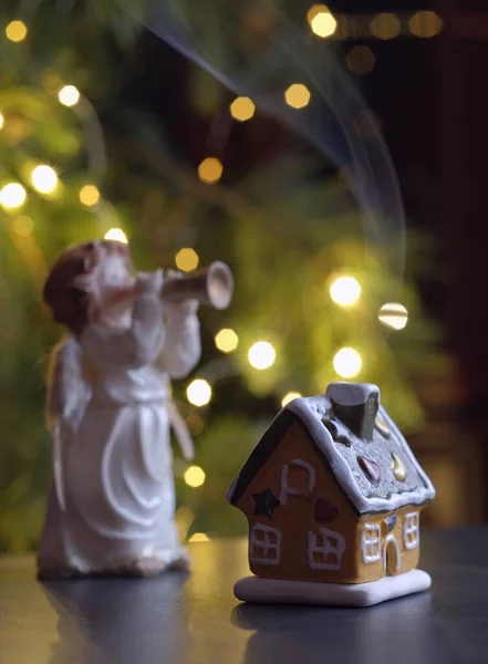 Bir Noel meleğinin arka planında bacadan çıkan dumanla seramik bir ev ve çelenkli bir Noel ağacı. İç kısımda Noel dekorasyonu