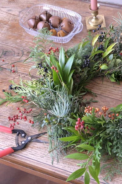 Çiçekçinin masasındaki yapım sırasında yeşil dallardan, ağaçların meyvelerinden ve çalılardan yapılmış Noel çelengi.
