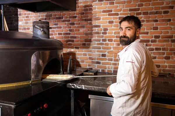 Pita turtalarını fırına koyarken Aşçı Kameraya Bakıyor