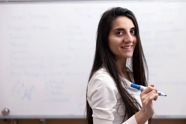 Beyaz Tahta Önünde Kalemle Kameraya Gülümseyen Bayan Öğretmen