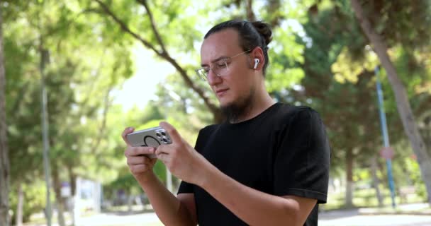 Молодий Чоловік Окулярах Дивиться Відео Телефоні Міському Парку Випрямляє Волосся — стокове відео