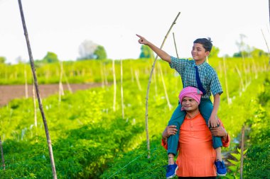 Hintli çiftçi ve oğlu tarım tarlasında, baba ve oğul çiftlikte duruyorlar, başarılı bir şekilde ektikleri ve günbatımının tadını çıkardıkları için mutlular.
