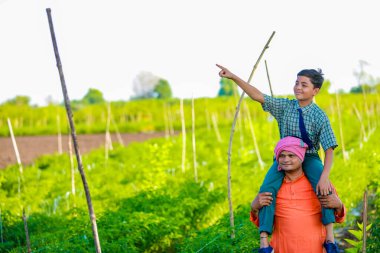 Hintli çiftçi ve oğlu tarım tarlasında, baba ve oğul çiftlikte duruyorlar, başarılı bir şekilde ektikleri ve günbatımının tadını çıkardıkları için mutlular.
