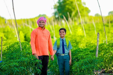 Şirin Hintli çiftçi çocuk. Okul üniformalı. Babası tarlada, mutlu baba ve oğlu.