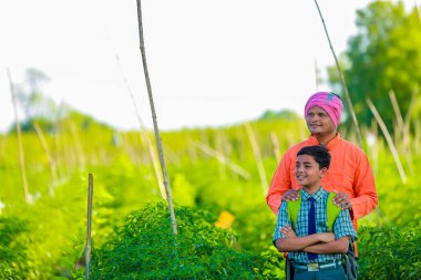Şirin Hintli çiftçi çocuk. Okul üniformalı. Babası tarlada, mutlu baba ve oğlu.