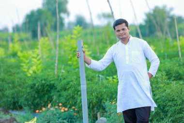 Mutlu Hintli çiftçi, elinde boruyla kameraya bakıyor.