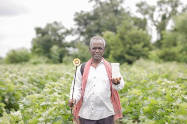 Çiftlik arazisinde çalışan Hintli çiftçi toprağa ve bitkilere gübre püskürtüyor. Zavallı çiftçi, mutlu çiftçi, yaşlı çiftçi.