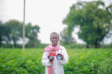 Hintli çiftçi kredi ve bankacılık için mini traktör oyuncağı tutuyor, fakir ve yaşlı çiftçinin başarısı