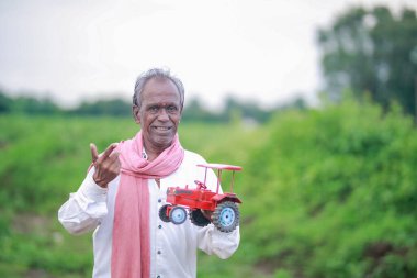 Indian farmer holding mini tractor toy for loan and banking , success of poor and old farmer clipart