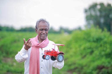 Indian farmer holding mini tractor toy for loan and banking , success of poor and old farmer clipart