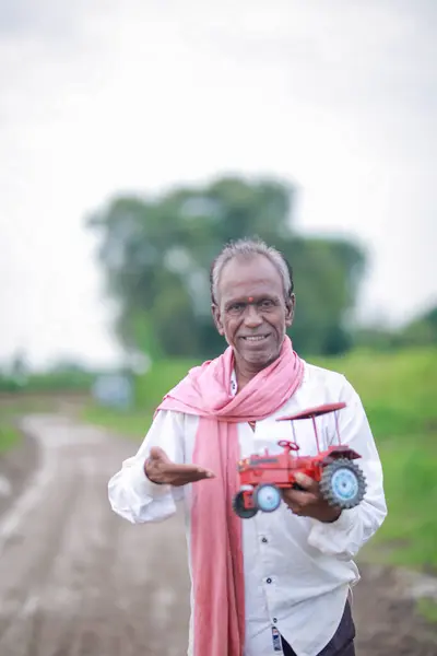 stock image Indian farmer holding mini tractor toy for loan and banking , success of poor and old farmer