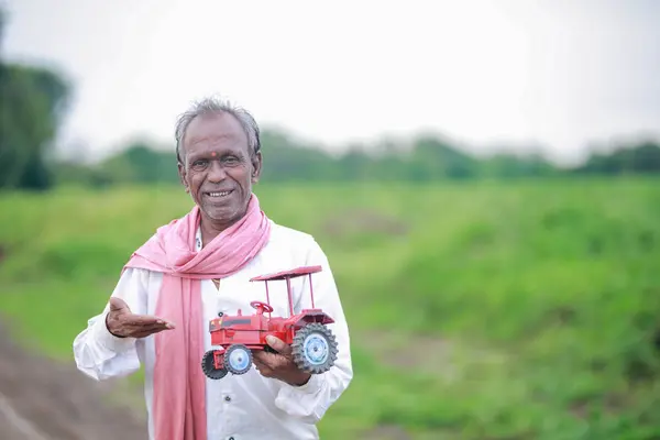 stock image Indian farmer holding mini tractor toy for loan and banking , success of poor and old farmer